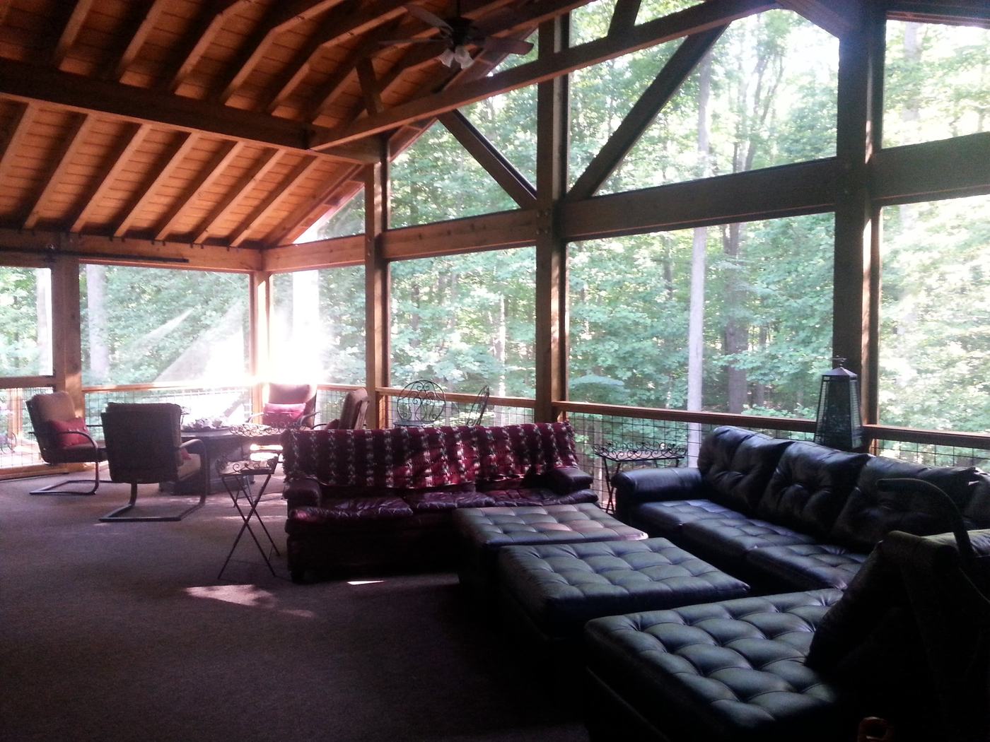 Inside the finished screened porch: exposed timber trusses, wood ceiling, screened walls and big leather sofas