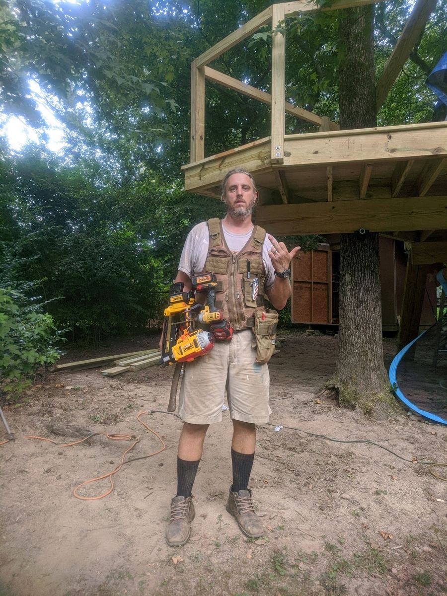 Mike Scott in his tool belt standing under the framed treehouse platform