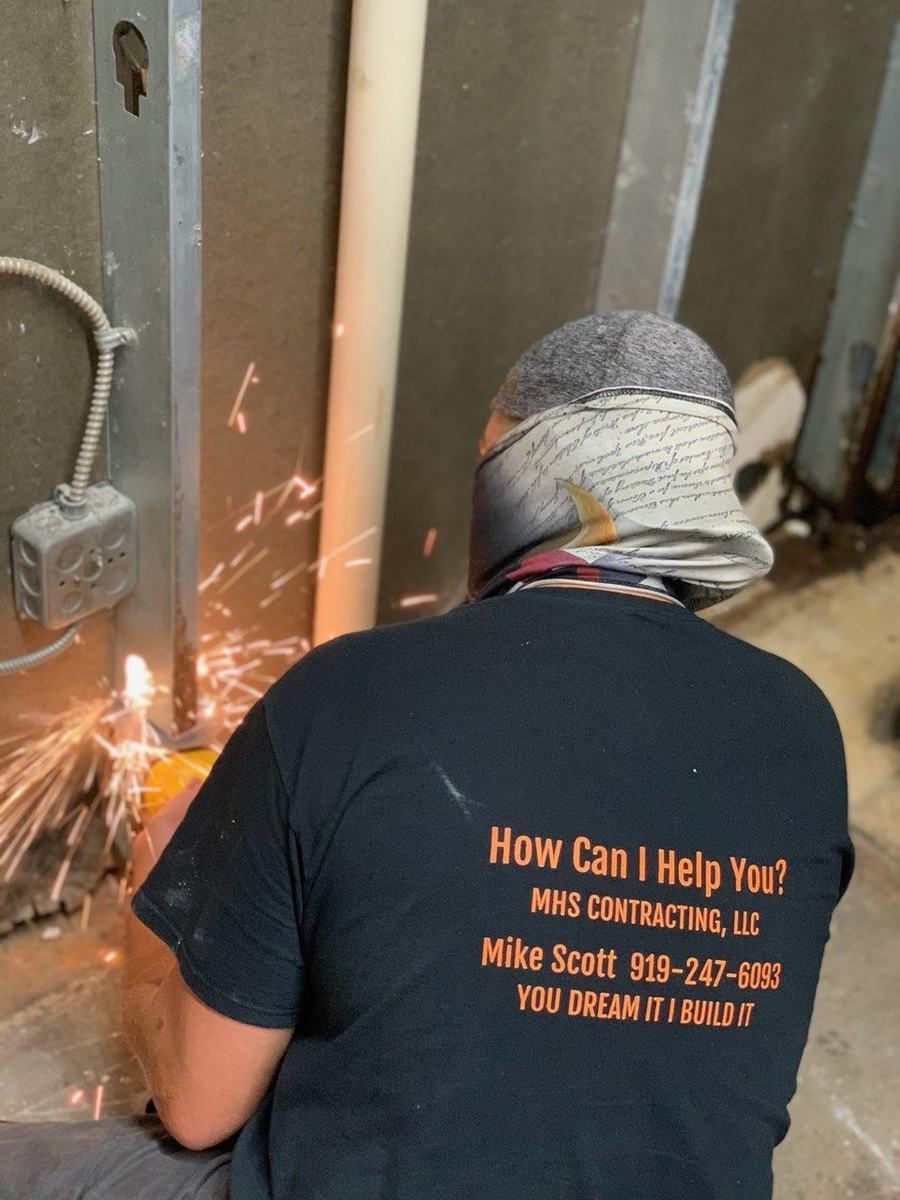Mike Scott cutting metal on a job site, wearing his MHS Contracting shirt that reads “You dream it, I build it”