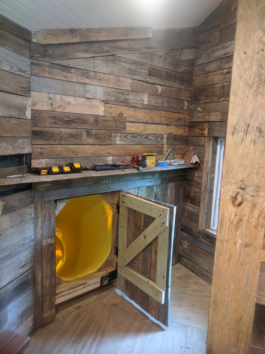 Playroom nook with reclaimed-wood walls and a yellow slide hidden behind a little barn door