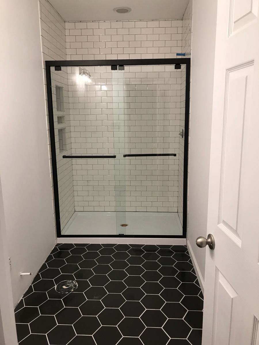Walk-in shower with white subway tile, black hexagon floor tile and black-framed glass door